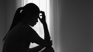 Silhouette of a distressed woman sitting by a window with her hand on her forehead, representing the emotional harm and personal suffering often involved in intentional tort cases.